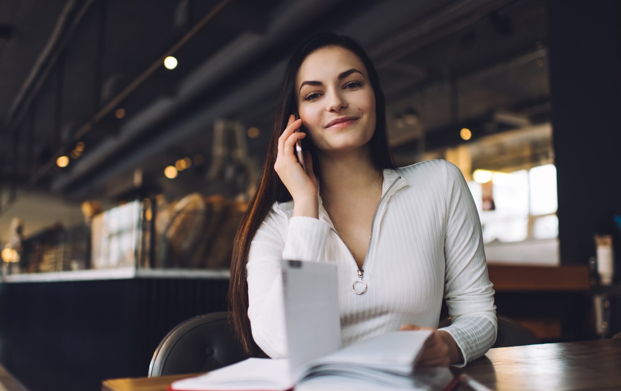 Smiling happy woman receiving call on smartphone at table