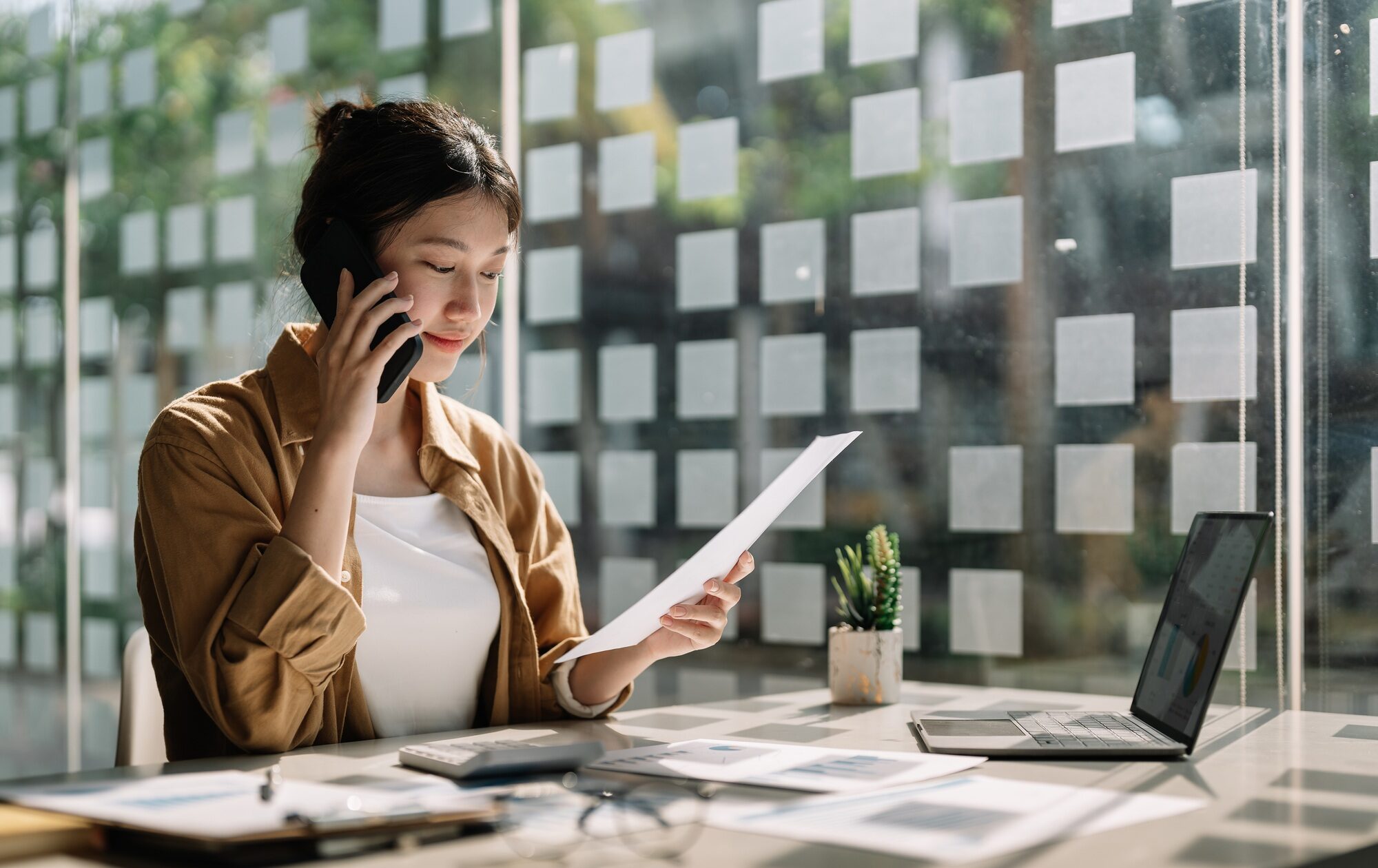 Young asian accountant calling marketing consultants and using laptop computer to analyze sales