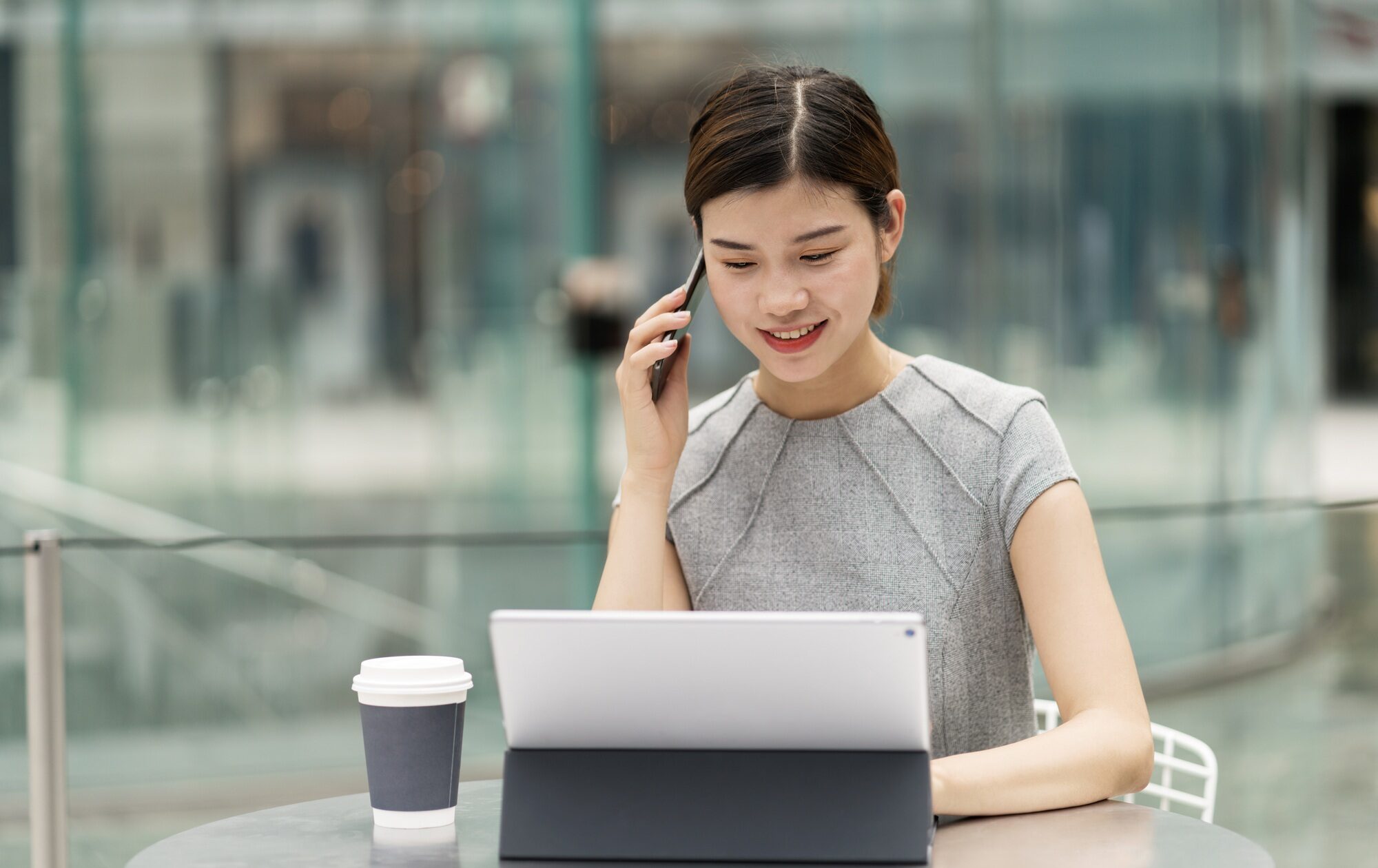 Young city businesswoman making smartphone call from sidewalk cafe